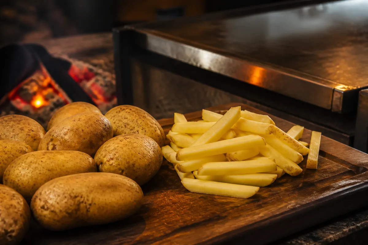 Pommes de terre entières et bâtonnets fraîchement taillés sur une planche en bois