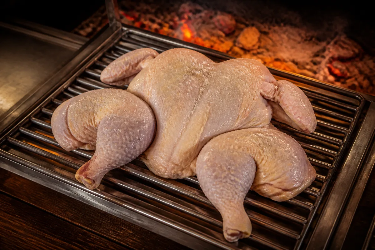 Poulet entier ouvert en crapaudine sur une grille, peau salée et sèche avant cuisson